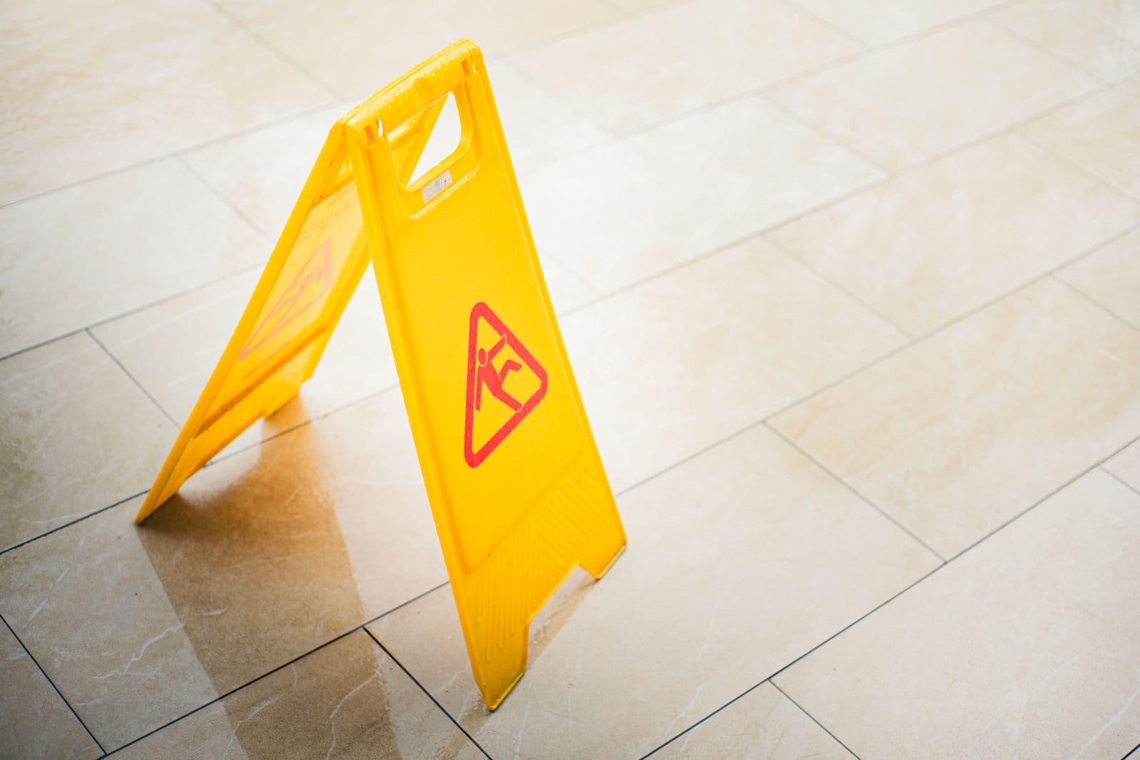 Yellow wet-floor caution sign on a tiled floor — moisture is the first suspect in coating failure